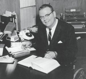Mike McBurney reading and writing at his office desk in 1960s