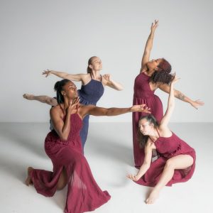 Four female presenting dancers from the Urban Jazz Dance Company are posed in different dance positions.