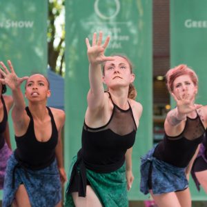 Zahna Simon and other female presenting dancers are lined up and reaching toward the camera during a dance.