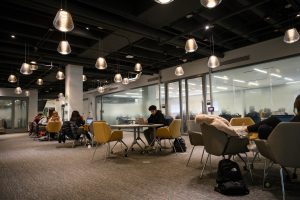 Students study in Grainger Hall, sitting at tables with laptops.
