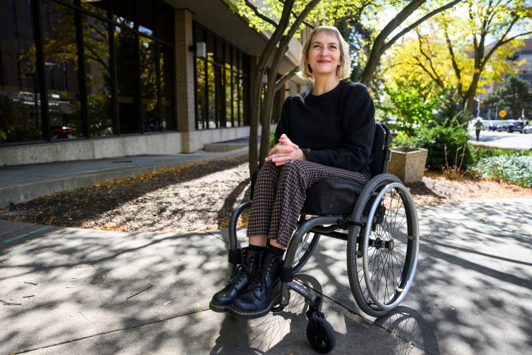 A photo of Rebekah Taussig seated in her wheelchair outside.